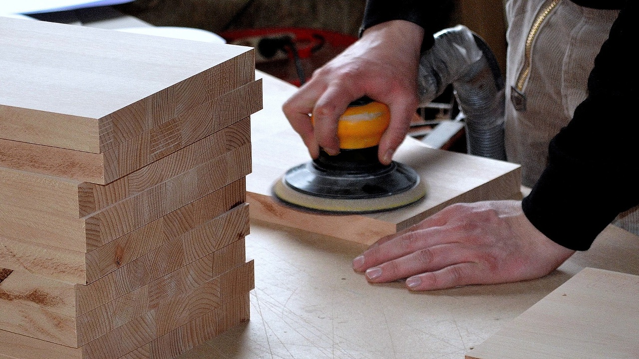 Eine Person schleift eine Holzplatte mittels Handschleifmaschine ab.